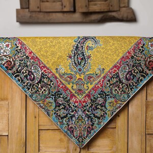 May include: A yellow tablecloth with a paisley pattern border. The tablecloth has a black, red, blue, and green paisley pattern. The tablecloth is on a wooden surface.