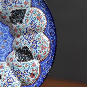 May include: A blue and white ceramic plate with intricate floral and geometric designs. The plate has a scalloped edge and is decorated with black, red, and green accents.
