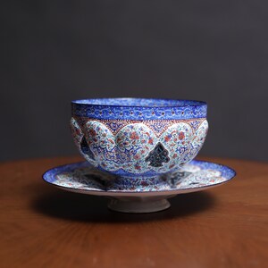 May include: A blue and white ceramic bowl with intricate floral and geometric patterns. The bowl is on a matching saucer with a raised base.