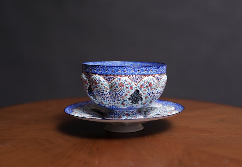 May include: A blue and white ceramic bowl with intricate floral and geometric patterns. The bowl is on a matching saucer with a raised base.