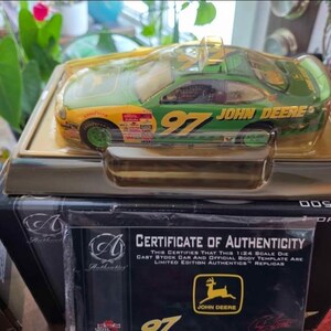 May include: A John Deere die-cast stock car model in a clear plastic case. The car is green and yellow with the number 97 and the John Deere logo. The model is a 1:24 scale replica and comes with a certificate of authenticity.