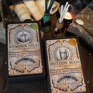 May include: Two black boxes with labels for pumpkin juice and buttery beer reed diffusers. The labels are decorated with vintage-style illustrations and text.
