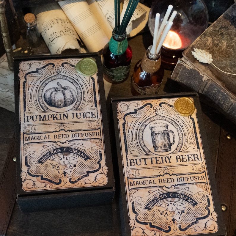 May include: Two black boxes with labels for pumpkin juice and buttery beer reed diffusers. The labels are decorated with vintage-style illustrations and text.