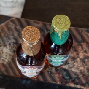 May include: Two glass bottles with brown liquid and labels. The bottles are sealed with wax, one green and one gold, with a raised image of a beer stein.