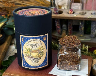 May include: A dark blue cylindrical container of Trelawney's Divination Tea, Vanilla flavour, with a decorative label. Beside it is a glass jar filled with loose tea leaves. The tea packaging has a celestial design with a teacup and flowers.