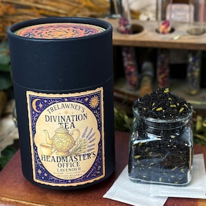 May include: A dark blue cylindrical container of Trelawney's Divination Tea, with a label featuring a teapot and the text "Headmaster's Office Lavender." A small glass jar holds loose tea. A tea bag is visible.