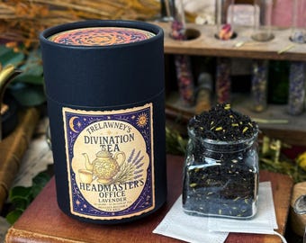 May include: A dark blue cylindrical container of Trelawney's Divination Tea, with a label featuring a teapot and the text "Headmaster's Office Lavender." A small glass jar holds loose tea. A tea bag is visible.