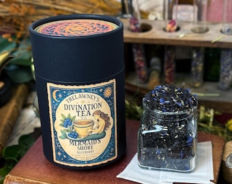 May include: A dark blue cylindrical container of Trelawney's Divination Tea, with a label featuring a mermaid and blueberries. A glass jar of loose leaf tea sits beside it. The tea is labeled "Mermaid's Shore Blueberry".