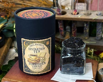 May include: A black cylindrical container of Trelawney's Divination Tea, with a label featuring a teacup and books. Beside it, a glass jar holds loose-leaf tea. The container's lid has a colorful, circular design. The tea is labeled "Forbidden Library Earl Grey".