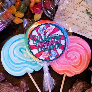 May include: Three colourful lollipops with a swirl design. The centre lollipop has a red, white and yellow striped design with the text "The Lonely Broomstick's Gigantic Enchanted Lollipop".