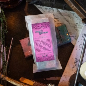May include: A pink and white wax melt bar with the text "The Lonely Broomstick Wax Melt Collection Happee Birthdae" and a description of the scent. Celebrate with our Happee Birthdae candle, scented with the nostalgic aroma of birthday cake. Embrace the sweet and joyful essence of freshly baked cake, complete with hints of vanilla and sugary delight. Perfect for bringing a touch of celebration and warmth to any birthday or special occasion.