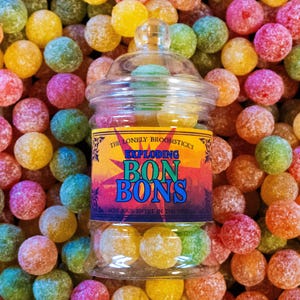 May include: A glass jar filled with colorful, round candies. The jar has a label that reads "The Lonely Broomsticks Exploding Bon Bons Don't Suck Sweets In The World".