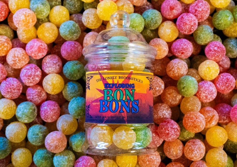 May include: A glass jar filled with colorful, round candies. The jar has a label that reads "The Lonely Broomsticks Exploding Bon Bons Don't Suck Sweets In The World".