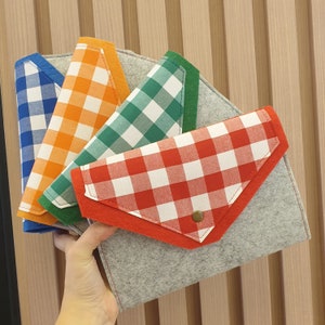 May include: Four fabric envelopes with different gingham patterns in blue, orange, green, and red. The envelopes are layered on top of each other and have a gray felt backing.