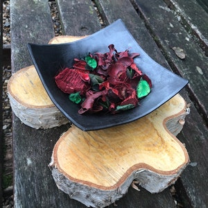 May include: A black square dish filled with red and green potpourri sits on a wooden slice. The dish is on top of a larger wooden slice.