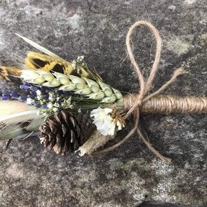 Op de afbeelding: Een klein boeket gedroogde bloemen gebonden met touw. Het boeket bevat lavendel, tarwe, witte bloemen, een dennenappel en een fazantenveer.