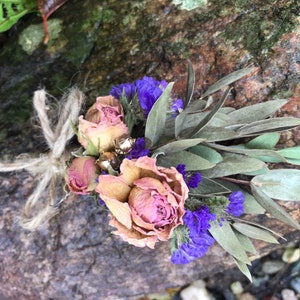 May include: A dried flower bouquet featuring pink roses, purple blooms, and green eucalyptus leaves tied with twine.
