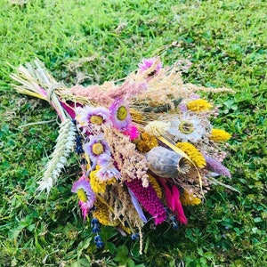 Pu&ograve; includere: Un bouquet di fiori secchi in tonalit&agrave; di rosa, viola, giallo e bianco. Il bouquet comprende erbe secche, baccelli di semi e altri elementi naturali.