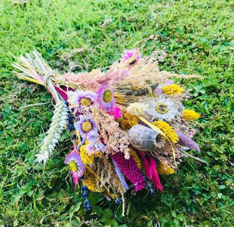 Pu&ograve; includere: Un bouquet di fiori secchi in tonalit&agrave; di rosa, viola, giallo e bianco. Il bouquet comprende erbe secche, baccelli di semi e altri elementi naturali.