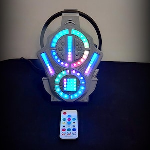 May include: A silver and gray light-up sound machine with a circular design and multiple colored lights. The machine has a remote control with buttons for different light settings.  The text on the remote control reads "RF Wireless".