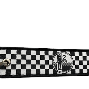 Puede incluir: Llavero a cuadros blanco y negro con un llavero plateado. El llavero presenta un logotipo blanco y negro con el texto "2 Tone".
