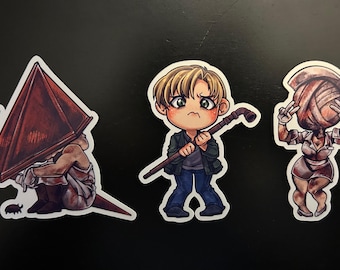 May include: Three cartoon stickers featuring characters from the Silent Hill video game series. The first sticker is of Pyramid Head, a humanoid figure wearing a large, pointed helmet. The second sticker is of James Sunderland, a man with brown hair and a worried expression. The third sticker is of a female character with a bandage wrapped around her head.