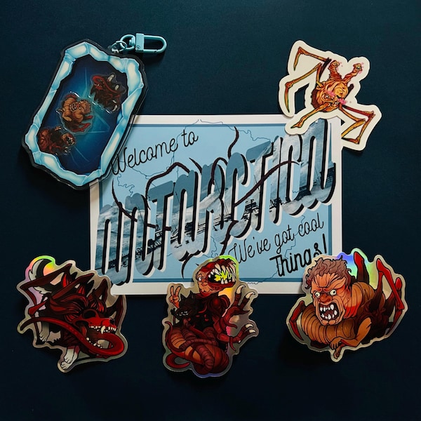 May include: A set of stickers featuring various creatures, including a dragon, a monster, and a crab. The stickers are holographic and have a blue background. The stickers are arranged on a blue surface with a postcard that says "Welcome to  " in a retro font. 