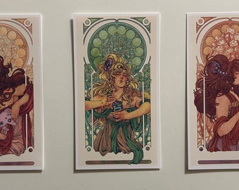 May include: Three art prints featuring women in Art Nouveau style frames. Each print features a woman with long hair and a flowing gown, holding a different object. The first print features a woman with brown hair holding a video game controller. The second print features a woman with blonde hair holding a can of soda. The third print features a woman with red hair holding a glass of wine.