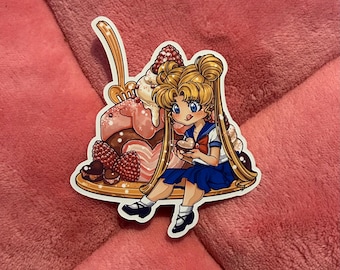 May include: A sticker featuring a cartoon character with blonde hair and a blue sailor uniform, sitting on a large dessert with chocolate, whipped cream, and raspberries. The character is holding a small chocolate heart.