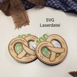 Può includere: Due portamonete in legno a forma di pretzel con la scritta "Oktoberfest" incisa. Ognuno contiene una banconota in euro piegata. Lo sfondo include un nastro di juta e un tessuto a scacchi blu e bianco.