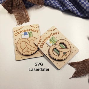 Può includere: Due porta carte regalo in legno a tema Oktoberfest. Ogni supporto presenta un design a pretzel tagliato al laser e la parola "Oktoberfest". I supporti sono marrone chiaro con piccoli pois e un design a banner nella parte superiore. Il testo "SVG Laserdati" è in basso.