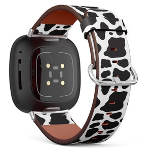 Könnte beinhalten: Eine schwarze quadratische Smartwatch mit einem weißen und schwarzen Kuhfell-Lederarmband. Das Armband hat ein braunes Lederfutter.