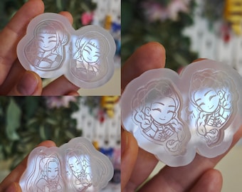 Könnte beinhalten: Transparente Silikonformen mit cartoonartigen Illustrationen von zwei lächelnden Frauen. Die Formen haben verschiedene Formen, jede mit detaillierten Gesichtszügen und Kleidungsdesigns. Das Thema deutet auf Bastel- oder DIY-Projekte hin, möglicherweise für Kunstharz.
