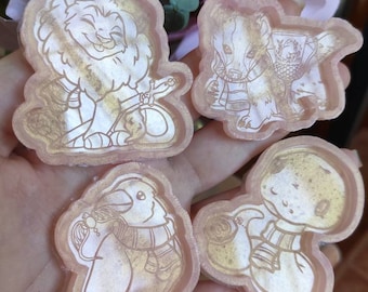 May include: Four resin-cast, gold-toned, animal-themed ornaments. The ornaments feature a lion, a badger, a bird, and a creature with a round head. Each ornament has a detailed design and a whimsical style.