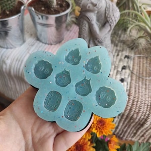 Puede incluir: Un molde de silicona azul claro con forma de flor. El molde tiene siete formas diferentes de personajes de la película animada El viaje de Chihiro. Los personajes incluyen Sin Cara, los espíritus de hollín y los espíritus del baño.