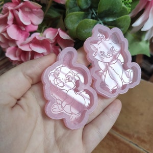 Op de afbeelding: Twee roze siliconen mallen, een in de vorm van een konijn en de andere in de vorm van een kat. Beide mallen hebben een witte omtrek van het dier erin.
