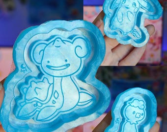 May include: Three light blue silicone moulds featuring embossed character designs. The largest mould depicts a creature with a shell, the top right mould shows a long-eared character, and the bottom right mould displays a stacked character design.