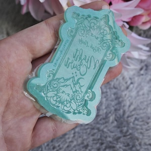 Peut inclure: Un moule en silicone bleu turquoise avec un cadre décoratif et des accents floraux. Le moule présente le texte "High Lady" et "Witchy Vibes".