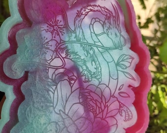 Puede incluir: Un molde de resina rosa y verde con un diseño de dragón y flores. El molde está hecho de silicona y está diseñado para fundir resina.