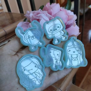 May include: Five clear blue resin charms featuring characters from the animated television series Adventure Time. The characters include Finn the Human, Jake the Dog, Princess Bubblegum, Marceline the Vampire Queen, and BMO.