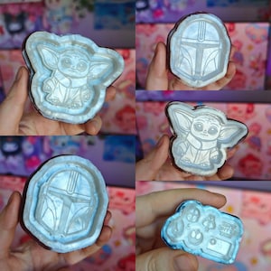 Pode incluir: Uma coleção de moldes de silicone com o tema Star Wars. Os moldes apresentam designs de Grogu, o capacete Mandaloriano e outros símbolos icónicos. Os moldes são azuis claros com uma borda castanha, perfeitos para projetos de artesanato.