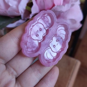 Puede incluir: Un molde de silicona rosa transparente con dos diseños de animales de dibujos animados. El molde está diseñado para crear amuletos de resina u otras artesanías.