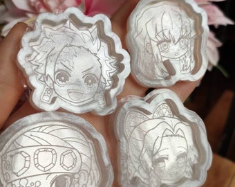 Könnte beinhalten: Vier transparente Harzformen mit erhabenen Umrissen von Anime-Charakteren. Die Charaktere sind im Chibi-Stil gehalten und haben große Augen. Die Formen befinden sich auf einer Hand.