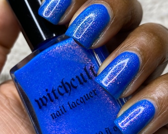 May include: A bottle of blue nail polish with a shimmery finish. The bottle is labeled "witchcult nail lacquer" and has a 0.50 fl oz capacity.