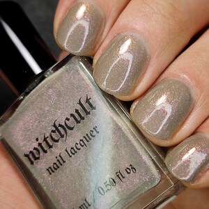 Puede incluir: Una botella de esmalte de u&ntilde;as Witchcult con un esmalte brillante marr&oacute;n claro en las u&ntilde;as. La botella est&aacute; etiquetada con "Witchcult nail lacquer" y "15 ml / 0.50 fl oz".