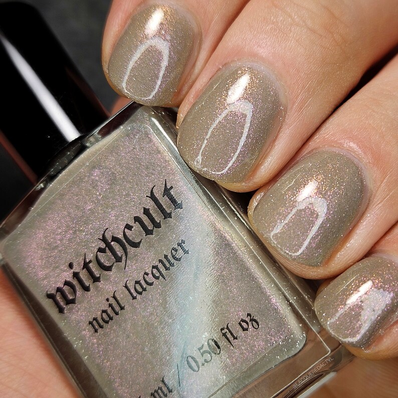 Puede incluir: Una botella de esmalte de u&ntilde;as Witchcult con un esmalte brillante marr&oacute;n claro en las u&ntilde;as. La botella est&aacute; etiquetada con "Witchcult nail lacquer" y "15 ml / 0.50 fl oz".