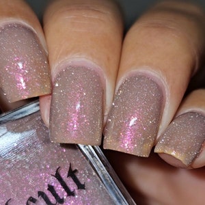Puede incluir: Primer plano de cuatro u&ntilde;as pintadas con un esmalte de u&ntilde;as marr&oacute;n claro con un fino brillo rosa. El frasco de esmalte de u&ntilde;as es visible en el fondo con la palabra "Cult" impresa en la etiqueta.