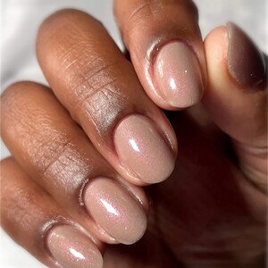 Puede incluir: Primer plano de una mano con esmalte de u&ntilde;as de color nude con un brillo sutil. Las u&ntilde;as son de forma ovalada y tienen un acabado brillante.