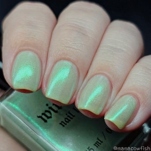 May include: A hand model wearing light green nail polish with a shimmery finish. The nail polish bottle is labeled "wild nail polish" and has a green label with black text.