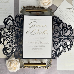 May include: Black and gold wedding invitation with a laser cut design. The invitation features the couple's names, "Gianna & Destin", and the wedding date, "The 24th of September".